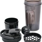 A disassembled black protein shaker bottle, including the main container, lid with spout, a twist cap, two mixing balls, and a grid insert, all placed on a flat surface.