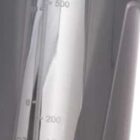 Close-up of a gray transparent container with measurement markings in milliliters and ounces. The measurements are printed vertically on the side up to 500 ml (16 oz). A light reflection is visible on the surface.