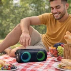 Man smiling at a picnic, touching Skylar Outdoor Bluetooth Speakers with colorful lights.