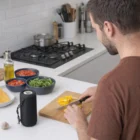 A man slices yellow bell pepper in a kitchen with Water-Resistant Bluetooth Speakers nearby.
