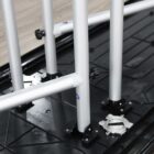 Close-up of several vertical metal poles attached to a black plastic base, secured with small knobs. The setup is on a light-toned wooden surface, likely part of a modular frame or stand system.