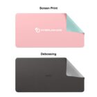 Two rectangular desk pads are shown. The top pad is pink with a screen-printed logo INTERLINKAGE, and has a corner folded to reveal a light blue underside. The bottom pad is dark gray with a debossed logo APIQ, with a corner folded to show a white underside.