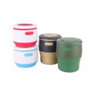 Four collapsible silicone cups are shown. Each cup has a lid and is designed in different colors: red and white, blue and white, black and tan, and green. They are stacked in two columns of two.