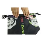 Hands folding a black bag with illustrations of skulls and text. The bag has clips on the side and features elements in white, red, and green.