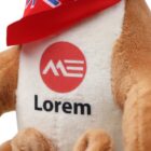 Close-up of a stuffed animal wearing a red, white, and blue bandana. The plush toy has brown fur and a white belly with a red circle logo and the text Lorem printed on it.