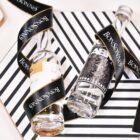 Two small liquor bottles are placed on a black and white striped surface. They are wrapped with a decorative black ribbon that has BONSONNO written on it in white.