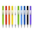 A row of ten ballpoint pens in various colors: green, red, orange, yellow, white, blue, and black. Each pen has a metallic clip and tip, and they are evenly spaced on a plain white background.