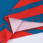 Close-up of fabric featuring blue and red geometric patterns and small dotted details. The fabric is folded to reveal stitching and layered material edges.