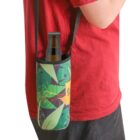 A person in a red shirt wears a beverage holder with a strap. The holder has a tropical leaf pattern and contains a beer bottle. The person stands facing right, with the holder hanging over their hip.