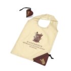 A cream-colored reusable shopping bag with Casterton Sedbergh Preparatory School printed on it, featuring a crest. Next to the bag are a small pouch with a similar crest and a matching brown pouch.