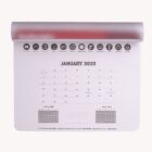 A wall calendar displaying January 2025 with icons and text above listing various products. Small calendars for December 2024 and February 2025 are at the bottom. The top has a red binding.