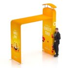 A man in a suit stands next to a large, orange promotional archway that reads World Emoji Day. The arch is decorated with smiling emojis and heart symbols.