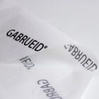A close-up of a white sheet of paper with the word GABRUEID® printed repeatedly in black text. The paper is slightly curved, showing parts of the print from different angles. The background is plain and white.