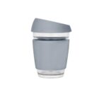 A gray reusable travel cup with a silicone sleeve and a tilted lid. The cup is transparent on the bottom half and gray on the top half, designed for hot beverages.