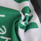 A close-up of a crumpled green and white fabric with partial white letters visible. The fabric appears smooth and the letters are partially obscured by the folds.