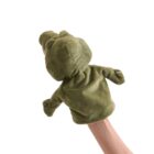 A green hand puppet resembling a dinosaur is being held up by a persons hand. The puppet has a round head and simple features, with small arms. The background is plain white.