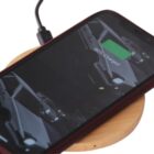 A smartphone with a red case is on a wooden wireless charging pad. The screen shows a car image and indicates the battery at 90% charged. A charging cable is connected to the pad.