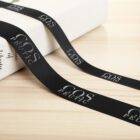 Black ribbon with the words COS PEUTIC printed in white, draped on a light wooden surface next to a white box.