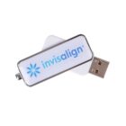 A USB flash drive with a white body and silver edges. It features the word invisalign in blue with a blue flower-like logo beside it. The cap is removed, revealing the USB connector.
