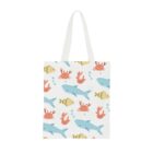 A white tote bag featuring a playful aquatic pattern with blue sharks, orange crabs, pink starfish, and yellow-green fish, interspersed with light blue bubbles. The design is scattered across the bag.