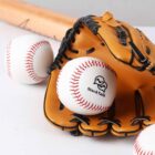 A brown baseball glove and two baseballs, one with StockTalk written on it, are placed on a white surface. A wooden bat is partially visible in the background.