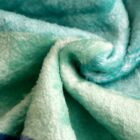 Close-up of a soft, teal blanket with a fluffy texture. The fabric is gently twisted, showcasing the plush and cozy material.