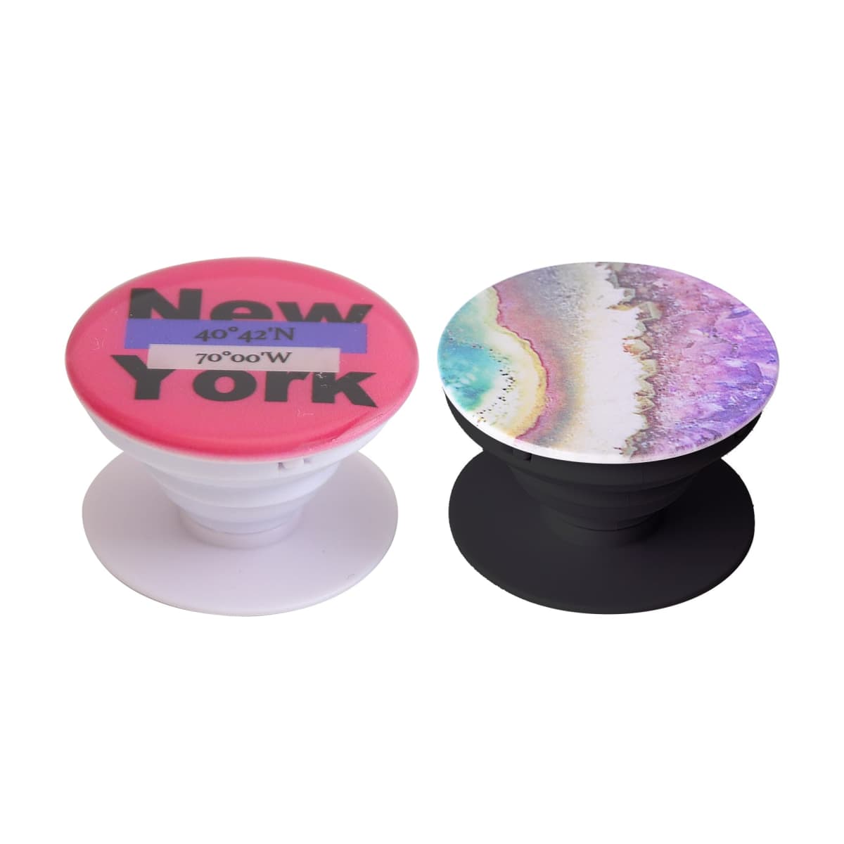 Two round phone grips are shown. The left one has a red top with New York and coordinates 40°42N 74°00W. The right one features a colorful abstract design resembling a beach with waves and sand.