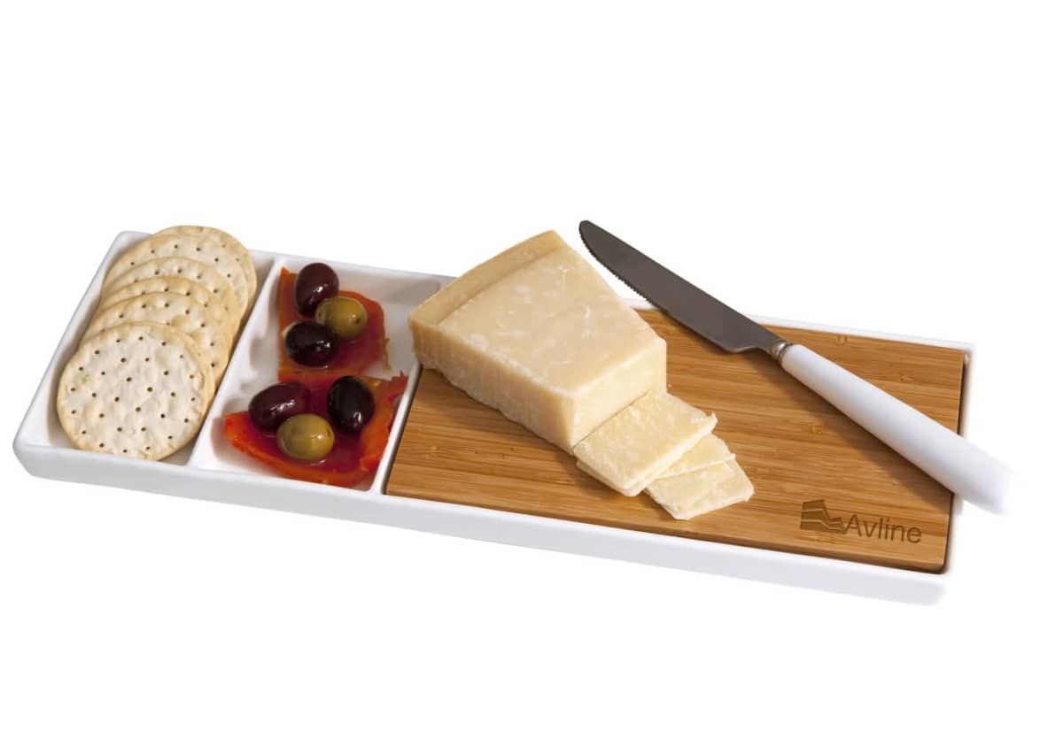 A cheese board with sliced cheese, a knife, crackers, olives, and red peppers arranged on a white tray with wooden accents.