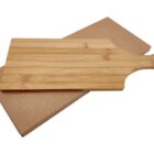 A wooden cutting board with a handle and a small hole at the end sits on top of a rectangular cardboard box. The board has a light, natural wood grain pattern.