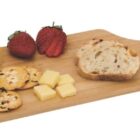 A wooden serving board with cheese wedges and cubes, thinly sliced bread, crackers, and two strawberries.