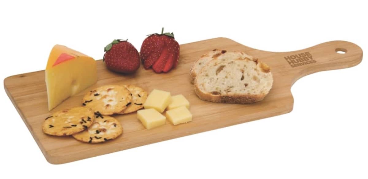A wooden serving board with cheese wedges and cubes, thinly sliced bread, crackers, and two strawberries.