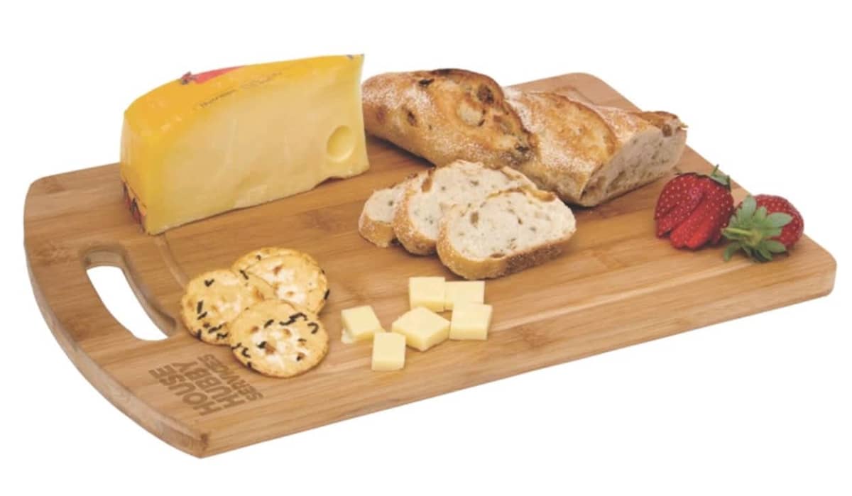 A wooden serving board with a block of yellow cheese, sliced bread, strawberries, crackers, and cheese cubes.