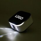 A small, square-shaped device with a black top displaying the word LOGO. It emits a beam of light from the bottom corner, casting a diagonal glow on the dark surface. The device has a sleek, modern design.