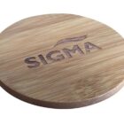 A circular wooden coaster with the word SIGMA and a stylized design engraved on the surface. The wood has a natural finish, displaying its grain pattern.