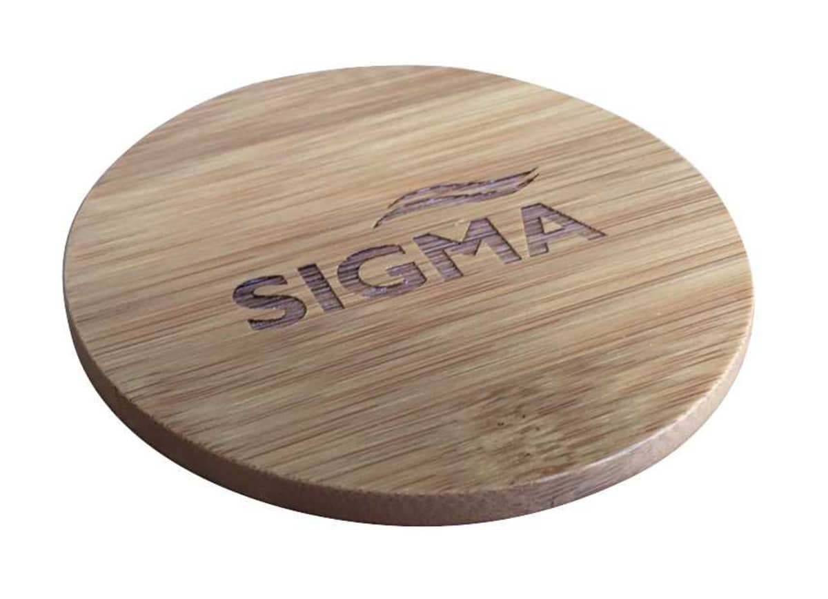A circular wooden coaster with the word SIGMA and a stylized design engraved on the surface. The wood has a natural finish, displaying its grain pattern.