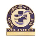 Gold and purple enamel pin featuring a cross with a stylized swoosh. The words Christus Spohn Hospital Alice Volunteer surround the cross in a circular design with rectangular base.