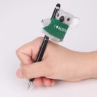 A hand holds a black pen with a plush koala attached. The koala wears a green vest with I ♥ AUSTRALIA printed on it.