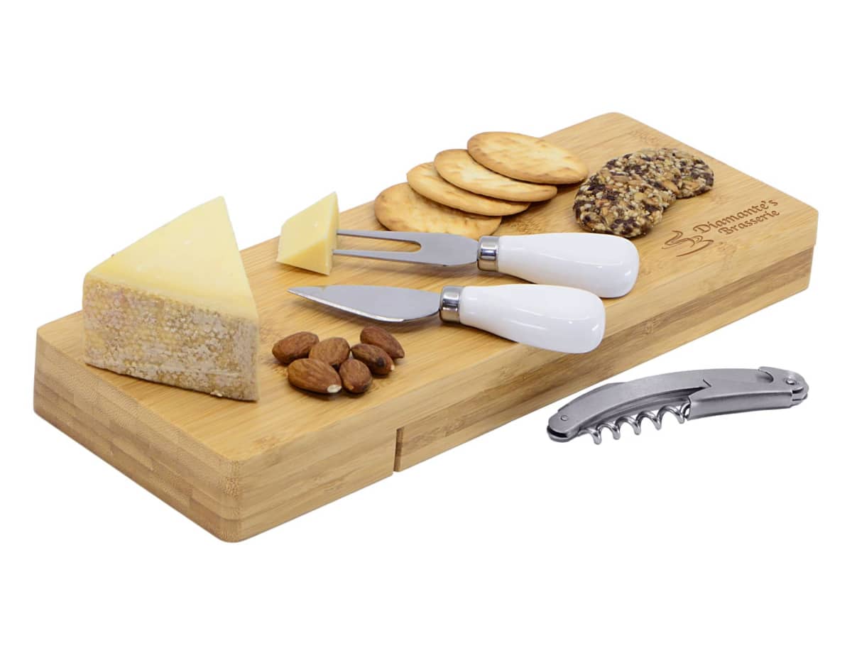 A bamboo cheese board with assorted cheeses, crackers, and almonds. Two cheese knives with white handles are on the board. A corkscrew lies beside it.