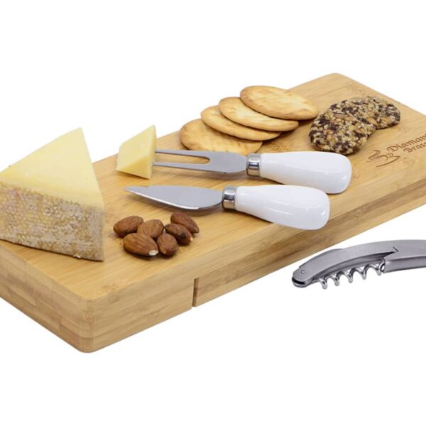 A bamboo cheese board with two cheese knives, sliced cheese, crackers, almonds, and a corkscrew.
