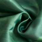 Close-up of emerald green silk fabric with a smooth, shiny surface. The fabric is folded and draped, creating soft curves and a sense of fluidity. The light reflects off the material, highlighting its luxurious texture.