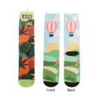 A pair of colorful socks with two designs. The packaging shows an abstract leaf and orange pattern. The socks display a landscape, featuring a hot air balloon, green hills, a brown path, and a sun. Labels indicate front and back views.