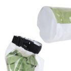 Close-up of a transparent dry bag with a black buckle strap, showing a green fabric inside. The bag is open at the top, revealing the white interior lining. The top view of the bag displays the circular white seal.