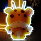 A cute cartoon character resembling an animal with orange spots and two small horns is illuminated. The character has a pink flower on its head and a smiling face, set against a dark background with some glow.