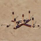 Wooden ring toss game set up on sand, featuring a cross-shaped base with five vertical pegs. A few rope rings are looped around the pegs, while others lie scattered nearby.