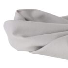 Close-up of a light gray fabric draped with gentle folds. The texture appears soft and smooth, with clearly visible stitching along the edge, indicating its quality and craftsmanship. The fabric has a matte finish.