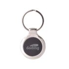 A round metallic keychain with a silver ring and a black circular center. The word doding is printed in white on the black center, along with a subtle graphic of a car.