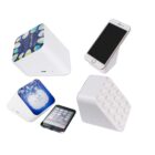 Four white, cube-shaped wireless speakers with various top designs are shown. Each is paired with a smartphone, resting at an angle on the speaker. Designs include a blue pattern, galaxy imagery, and building block-like dots.