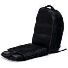 A black backpack is open, revealing two zippered compartments inside. The backpack is positioned upright, showing its sleek, smooth exterior and textured side panels. The zippers have a modern, streamlined design.