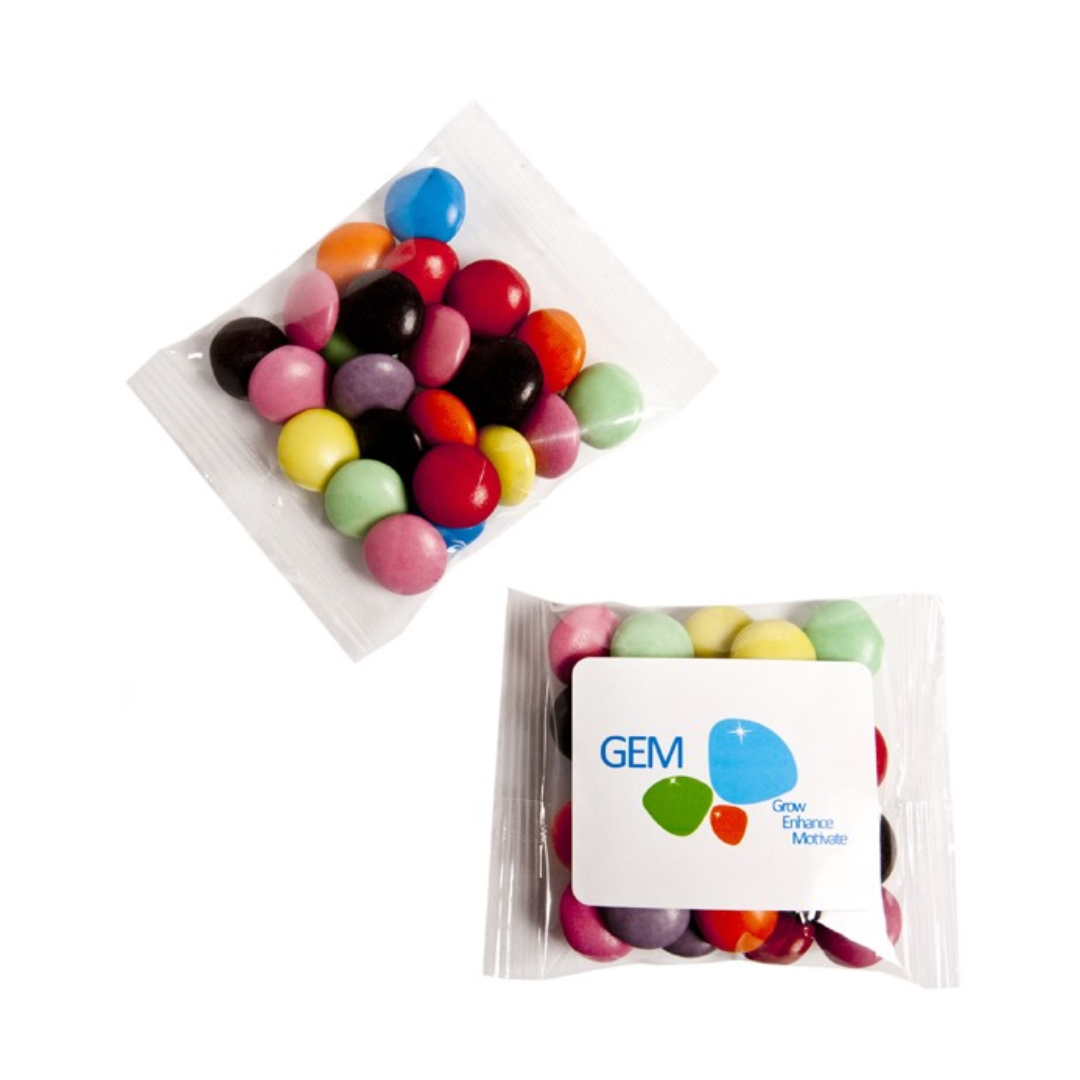 Two small plastic bags of colorful candy-coated chocolates, with one branded GEM, featuring Grow Enhance Motivate and vibrant stones. The Branded Pocket Chocolate Candy Bag offers the ideal treat to enjoy on the go!.