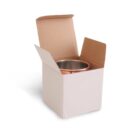 A cardboard box partially opened to reveal a copper or metallic container inside, standing on a white surface. The box has flaps bent outward, showing the contents.